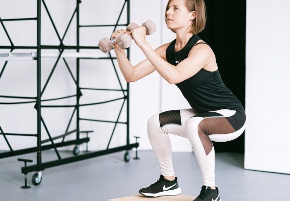 A woman in sportswear performs a squat with dumbbells indoors, embodying strength and healthy living.